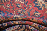 Folded vintage Persian Meshed rug displaying cochineal red field, navy scrolled tendrils, and visible knot heads.
