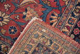 Vintage Meshed carpet corner, folded showing cochineal red pile, navy blue lotus flowers, beige border, and cream fringe.