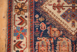 Antique Afshar rug with indigo field, tribal figures, geometric plant motifs, and cream border.