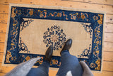 Antique Chinese Peking rug, central multi-petalled floral motif, ivory ground, and cobalt border.