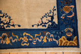 Corner detail of antique Peking rug: beige field, cobalt blue border with scrolling gold vinery, and tree branch motif.