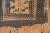 Lower corner of an antique Ningxia rug with visibly tattered fringe and blue-brown geometric border.