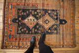 Geometric animal motifs and evident pile wear on a vintage Caucasian rug in navy and terra cotta.