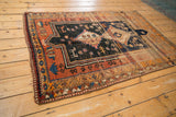 Vintage Caucasian rug's corner showing worn terra cotta, navy, and tangerine geometric border patterns.
