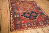 Vintage Caucasian rug corner, displaying red and navy geometric guls, stepped contours, and fringe.