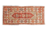 Distressed Oushak runner with pomegranate red floral medallion, beige field, and ribboned inner border.