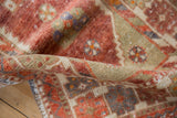 Distressed vintage Oushak rug fold revealing worn pile, playful floral motifs in pomegranate red and beige.