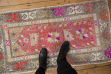 Distressed vintage Oushak rug with faded raspberry, ivory, and bright magenta patterns.