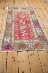 Distressed Oushak rug corner with raspberry red field and vibrant purple border patterns.