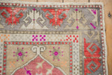 Distressed Oushak rug corner showing worn texture with fuchsia, red, and gray motifs.