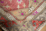 Folded distressed Oushak rug revealing textured pile, dusty raspberry, and beige floral motifs.