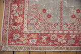 Distressed vintage Oushak rug corner showing red floral border, muted abrashed field, and visible wear.