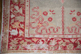 Distressed vintage Oushak rug corner showing cherry red floral palmette motifs and foundation wear.
