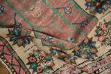 Folded vintage Oushak rug pile revealing even wear and floral motifs in mauve, emerald, and sapphire.
