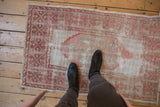 Distressed vintage Oushak rug with faded dusty rose, cochineal red, and ivory geometric patterns.