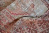 Close-up of distressed Turkish Oushak rug pile, showing rose, ivory, and cochineal red tones.