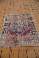 Distressed Oushak rug displaying geometric motifs and blossomed buds in purple, pink, and sand tones.