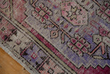 Corner of distressed vintage Oushak rug, revealing worn pile, visible foundation, purple, and pink hues.