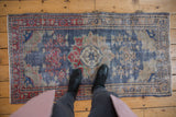 Distressed vintage Oushak rug with faded navy, red, and beige floral motifs, showing surface wear.