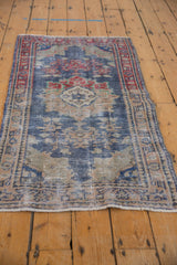 Distressed Oushak rug corner with faded cherry red border and worn navy florals.