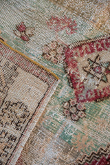 Detail of vintage distressed Oushak rug's worn pale mint green pile, ivory foundation, and corded selvage.