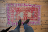 Vintage distressed Oushak rug corner with fuchsia geometric border, faded red floral field.