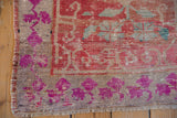 Distressed Oushak rug's fuchsia floral border, fringe, and visible even pile wear.