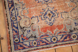 Worn corner of the Distressed Oushak rug, with short fringe and faded red, blue motifs.