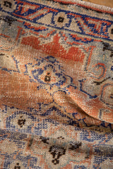 Faded brick red and cobalt blue motifs on a distressed Oushak rug's textured pile.
