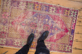 Vintage distressed Oushak rug in faded pink, purple, and gold with feet.