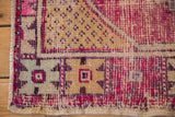 Distressed vintage Oushak rug corner showing wear, pink, purple, and saffron floral motifs.