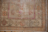 Distressed Oushak rug corner showing wear, intricate roundel border motifs, and faded blush, copper, beige tones.