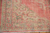 Distressed corner detail of vintage Oushak rug with faded pink, ivory, green patterns and visible wear.