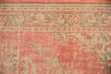 Distressed pink Oushak carpet pile texture with a faded ivory and green border.