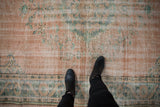 Distressed vintage Oushak rug showing worn blush field, faded green floral motifs, and boots.
