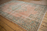 Distressed vintage Oushak corner with faded blush field, mint patterns, and foundation showing through.