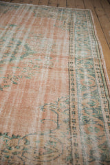 Distressed Oushak rug with low pile texture, faded blush field and mint green border.
