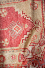 Folded detail showing the soft, worn texture of a vintage Oushak rug in dusty raspberry tones.