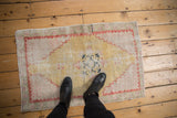 Distressed vintage Oushak rug with dusty gold field, pale brick red border, and blue central motif.