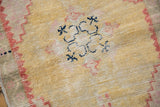 Distressed texture of a vintage Oushak rug, dusty gold, faded brick red, dark blue motifs.