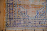 Distressed Oushak rug corner showing worn pile, short fringe, and geometric border in tangerine, dusty navy.