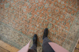 Distressed vintage Oushak rug with pale terra cotta scrolling vinery field and ivory vine border.