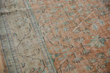 Traditional distressed Oushak field with scrolling vinery in pale terra cotta, ivory, and blue-green.