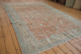 Distressed Oushak carpet corner, with pale terra cotta field, meandering vine border, and fringe.