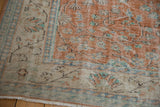 Corner of a distressed vintage Oushak rug, showing faded terracotta field, ivory border, and fringe.