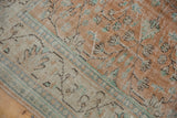Distressed Oushak rug showing pale terra cotta field with scrolling vinery and ivory meandering border.