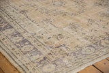 Distressed Oushak carpet showing worn beige pile, faded blue floral motifs, intact selvage.