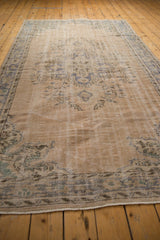 Distressed Oushak rug corner showing intact selvage, short fringe, and faded blue-green border.