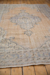 Distressed vintage Oushak rug pile with sand and faded blue curvilinear motifs.