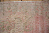 Distressed pile of vintage Oushak rug showcasing faded blush, ivory, and seafoam green.